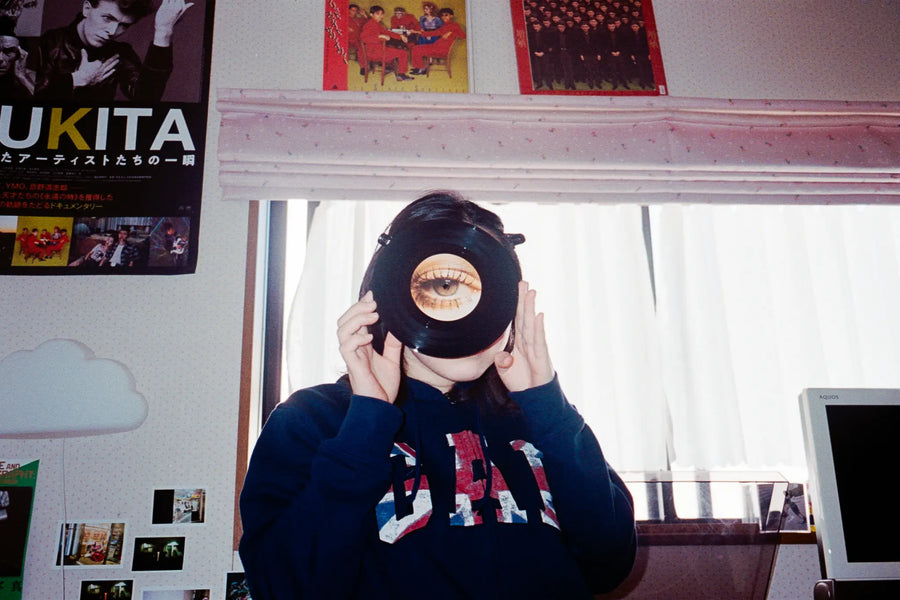 A person holds a record with an eye on its label in front of their face, surrounded by music posters.