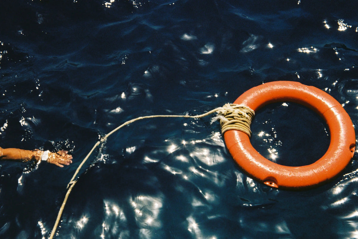 An orange lifebuoy and a rope floating on dark water beside a pier.