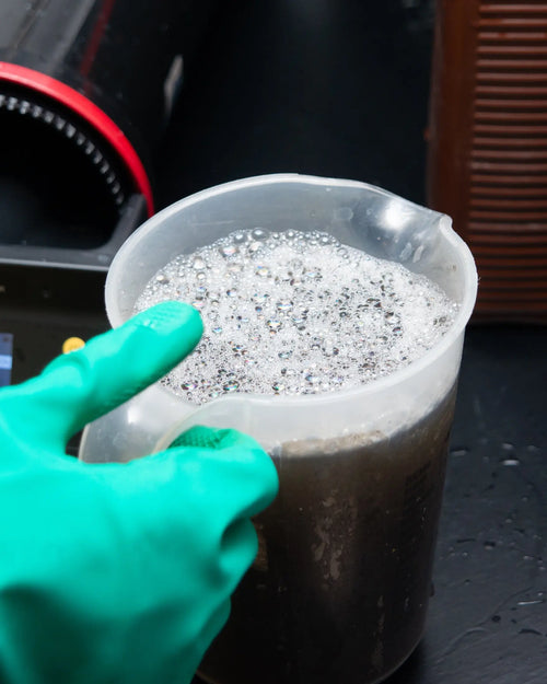 Gloved hand holding a measuring jug beside the AGO processor at Berlin Photo Studio